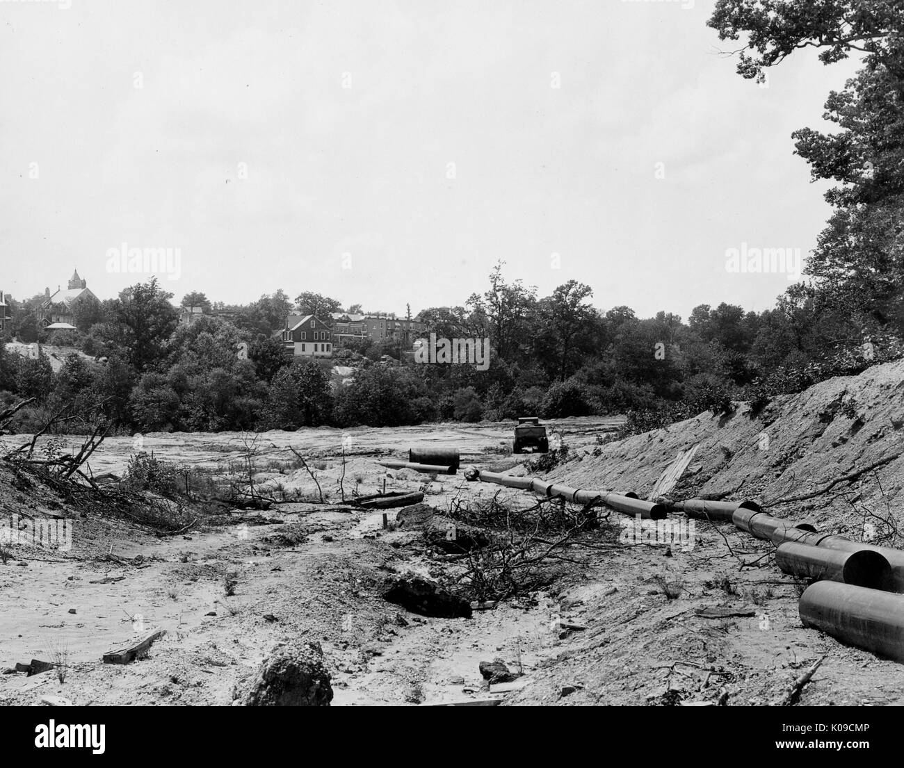 Northwood neighborhood land under construction, there are large pipes scattered on the uneven dirt, there are trees and houses in the background that are bordering the land, United States, 1950. Stock Photo