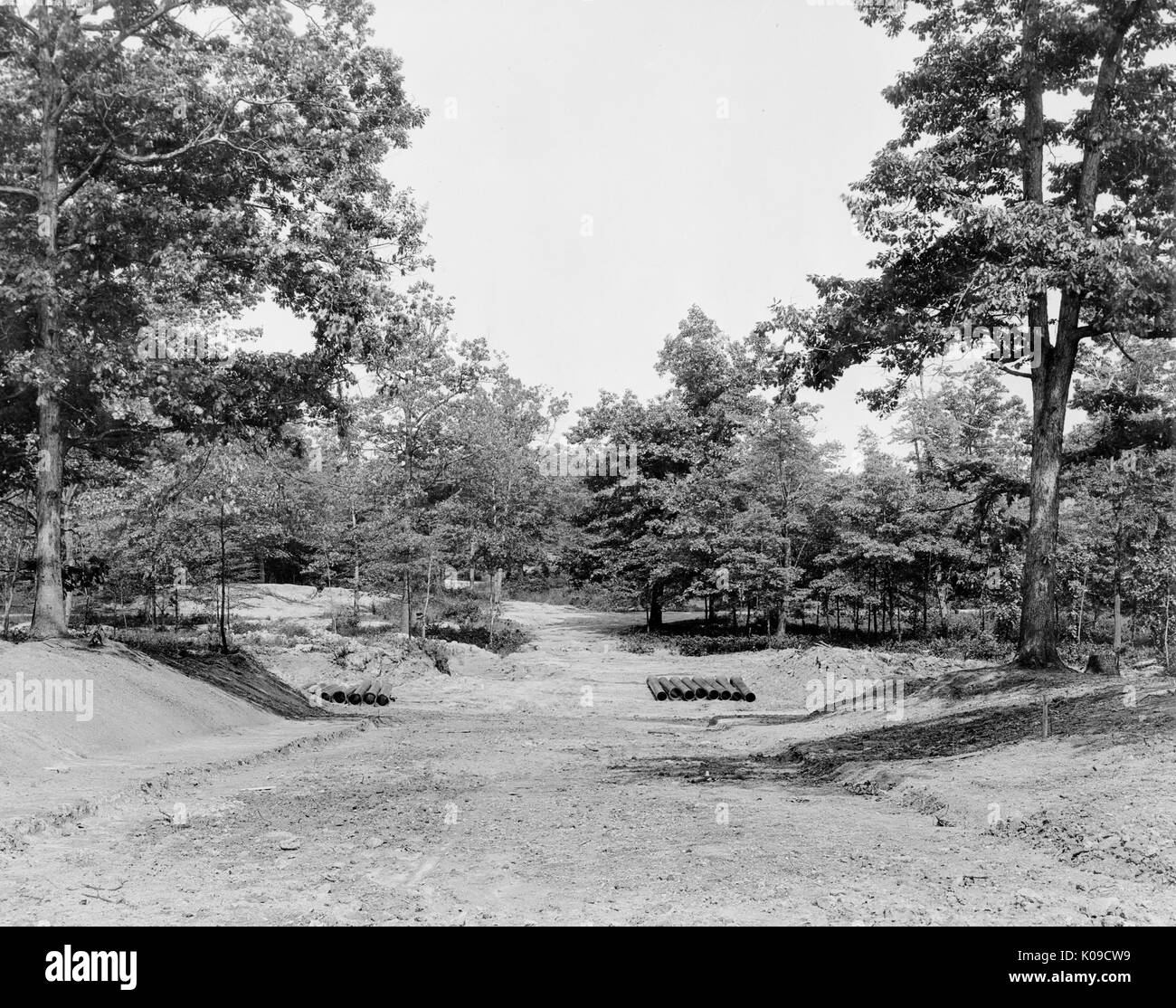 View of a construction site in Baltimore's Northwood neighborhood, the land is elevated in the foreground and declines towards the background, there are rows of utility pipes at the base of the decline and trees border the area, United States, 1950. Stock Photo