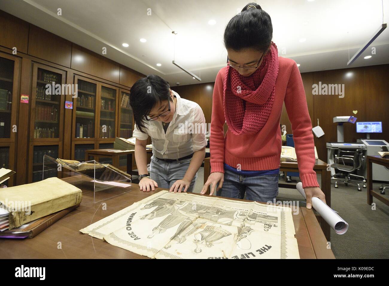 Two female college students are looking down at a large illustration artifact at the library event called Dirty Books and Longing Looks, February 11, 2016. Stock Photo