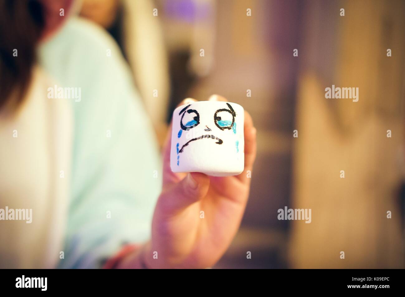 Soft focus photograph of a student holding a marshmallow with a crying face drawn onto it, October 31, 2015. Stock Photo