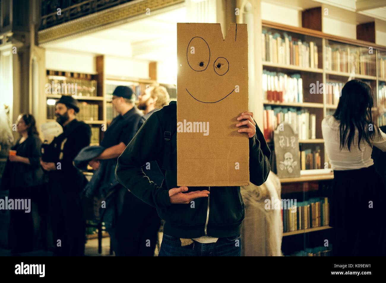 A student shown holding up the Plank from the television show 'Ed, Ed, n Eddy'; party-goers shown in the background with the library stacks, Halloween at Peabody, October 31, 2015. Courtesy Eric Chen. Stock Photo