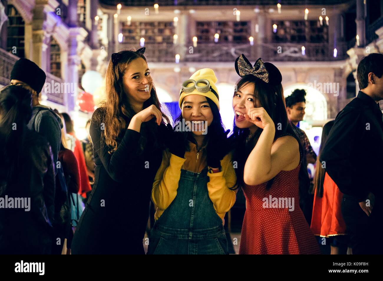 Three college students in costume pose for a photo, the girl on the far left is dressed as a black cat, the girl in the middle is dressed as a minion from the movie 'Despicable Me' and the girl on the far right is wearing a red dress and a black bow on her head, 2016. Stock Photo