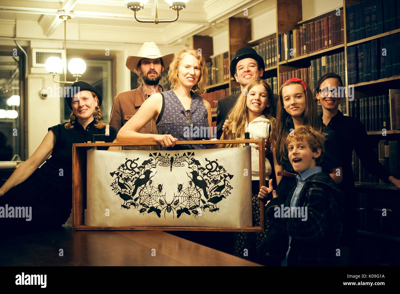 Several adults and three children are posing behind a large artifact, the artifact is a symmetrical drawing that is rolled between a wooden frame, 2015. Courtesy Eric Chen. Stock Photo