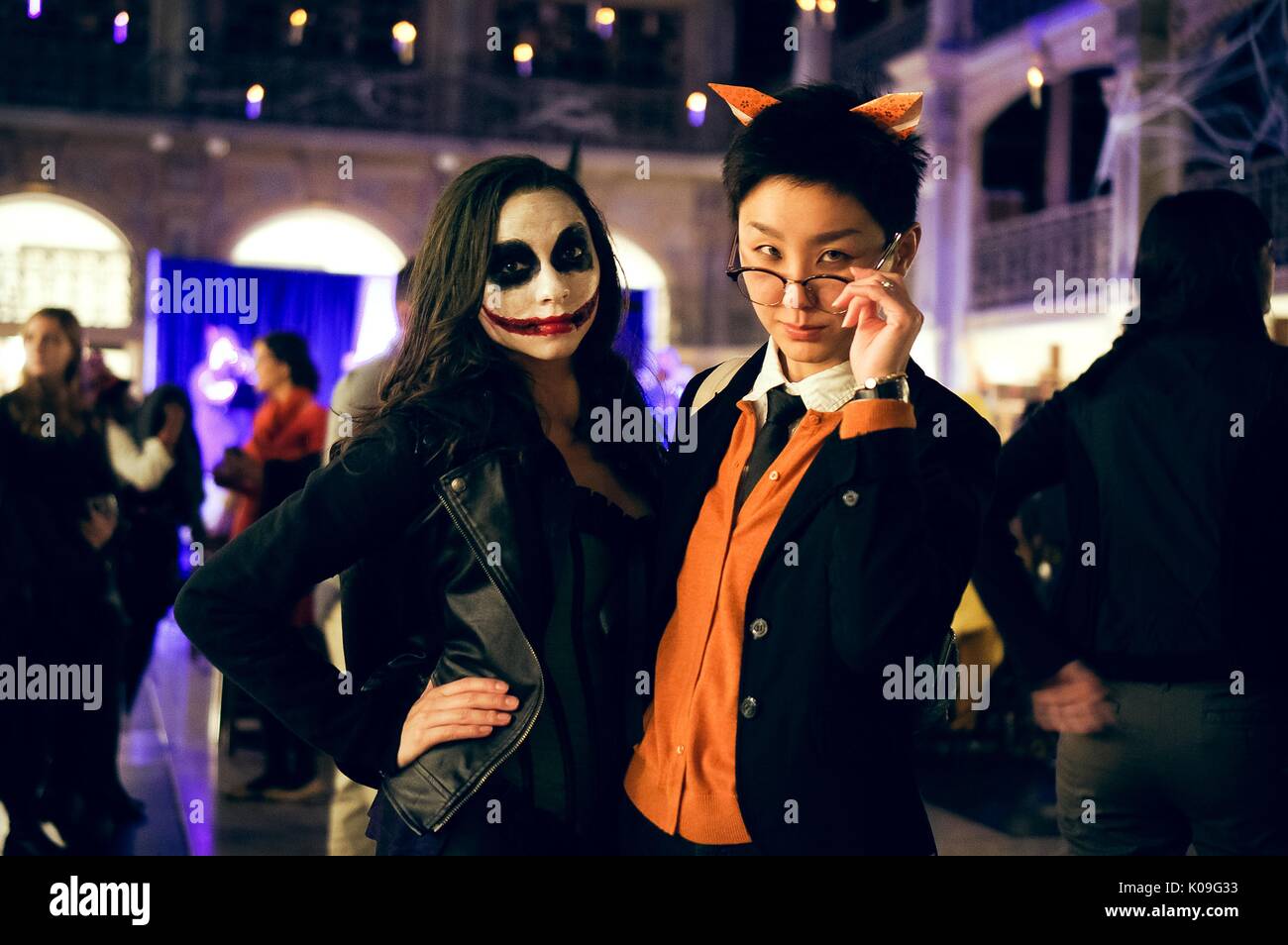 Two college students posing with their arms around each other, the girl is wearing all black and has face makeup on in the style of the character The Joker, she has a large red smile and black around her eyes and the boy is wearing orange ears, glasses and an orange and black outfit, 2015. Courtesy Eric Chen. Stock Photo