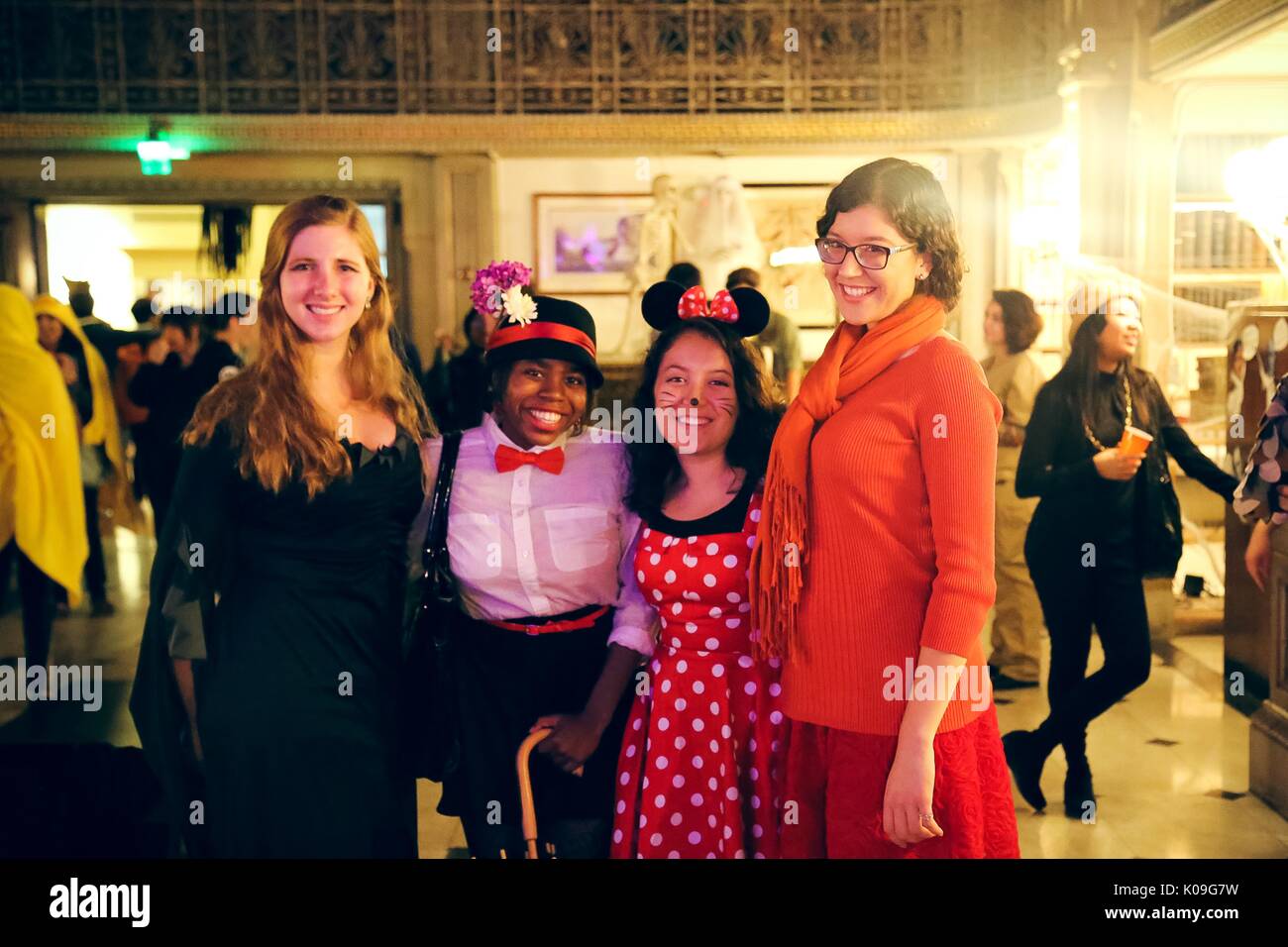 Four female college students are posing and smiling, the girl on the far left is wearing a black dress, the next girl is dressed as Mary Poppins and is holding an umbrella, the girl next to her is dressed as Minnie Mouse and the girl on the far right is dressed as a Wilma from Scooby Doo, 2015. Courtesy Eric Chen. Stock Photo