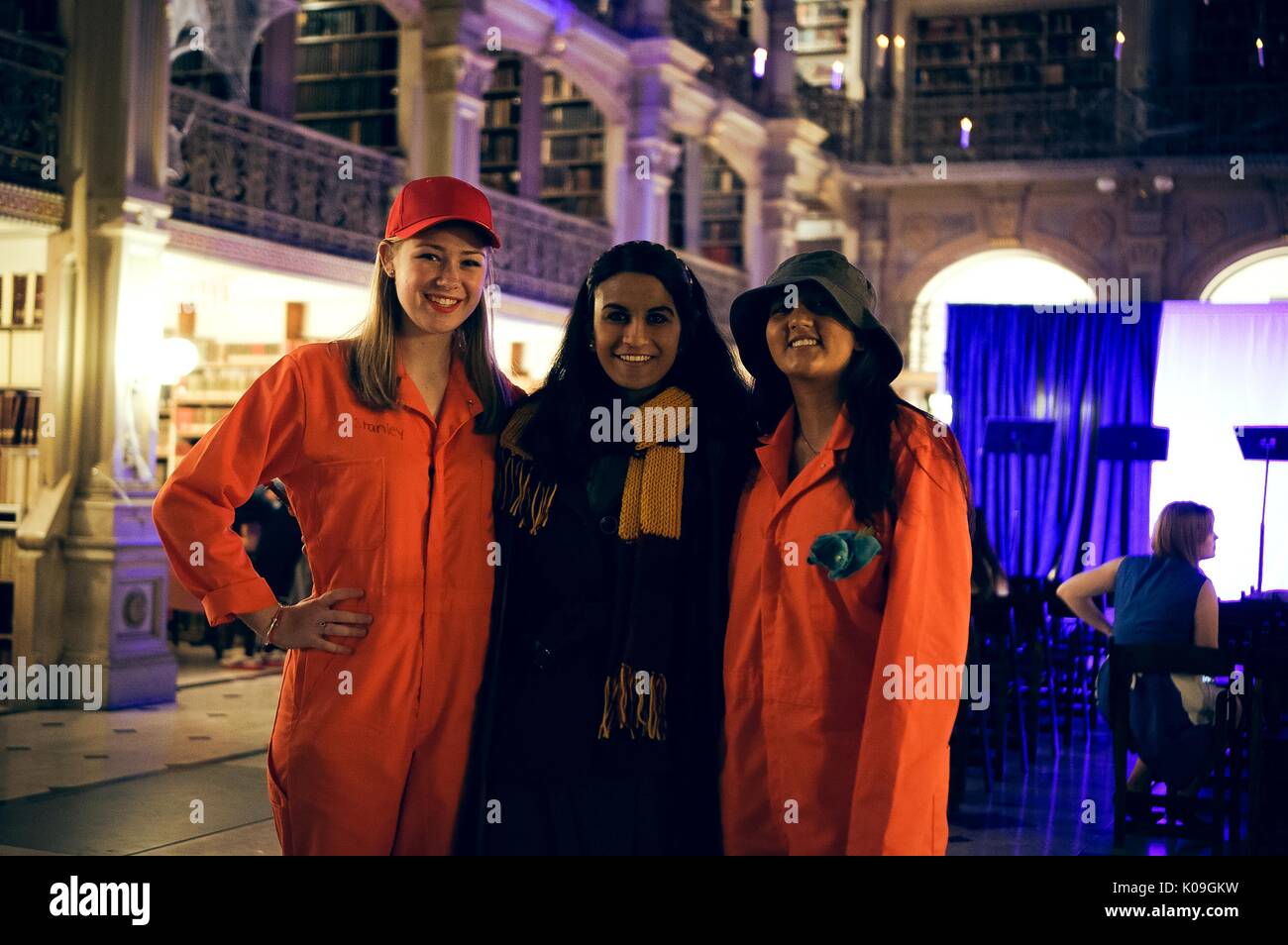 Three college students are posing for a picture, the two girls on the end are wearing orange jumpsuits and hats in order to portray characters from the story 'Holes' and the girl in the middle is wearing a scarf and is dressed as a Harry Potter character, 2015. Courtesy Eric Chen. Stock Photo