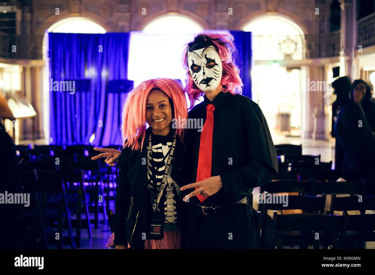 Two college students are posing for a picture, the girl is wearing a pink wig and a shirt with a skeleton's body on it while the boy is also wearing a pink wig, he is also wearing a face mask, a full black outfit and a red tie, Halloween at Johns Hopkins University's George Peabody Library, 2015. Courtesy Eric Chen. Stock Photo