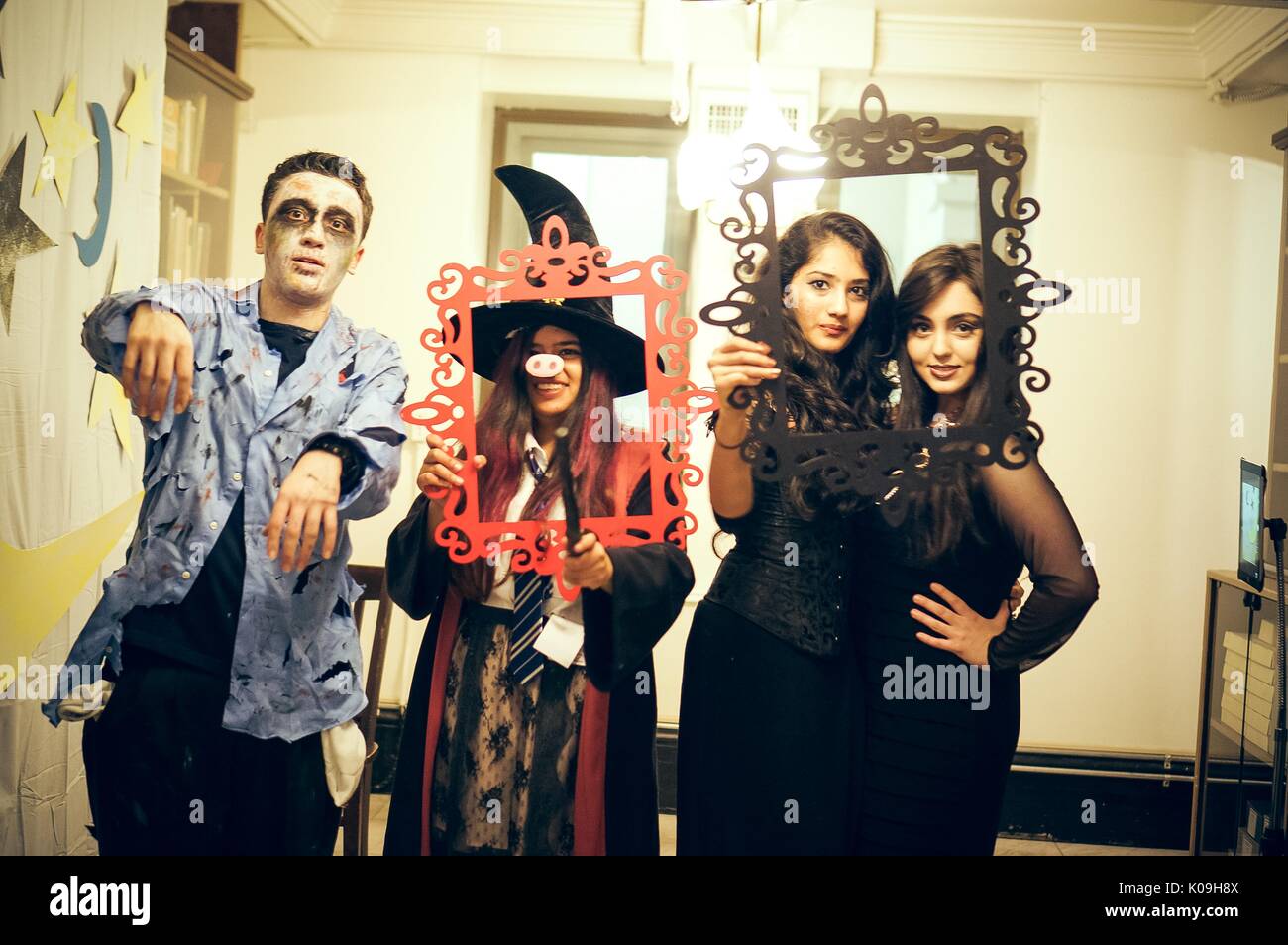 Four students in costume pose for a picture, one male student is dressed as a zombie, one girl is dressed in a witch costume with the nose of a pig and is holding a wand, and the other two girls are wearing black dresses, the girls are holding picture-frame props to outline their faces, 2015. Courtesy Eric Chen. Stock Photo