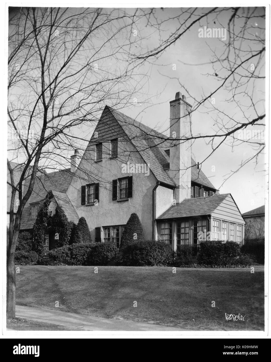 Photograph of a three-story home in Guilford neighborhood in Baltimore, with a cleanly cut grass and shapely bushes in front of the home with angular roofs and a plain facade with no use of bricks, Baltimore, Maryland, 1935. This image is from a series documenting the construction and sale of homes in the Roland Park/Guilford neighborhood of Baltimore, a streetcar suburb and one of the first planned communities in the United States. The neighborhood was segregated, and is considered an early example of the enforcement of racial segregation through the use of restricted covenants. Stock Photo