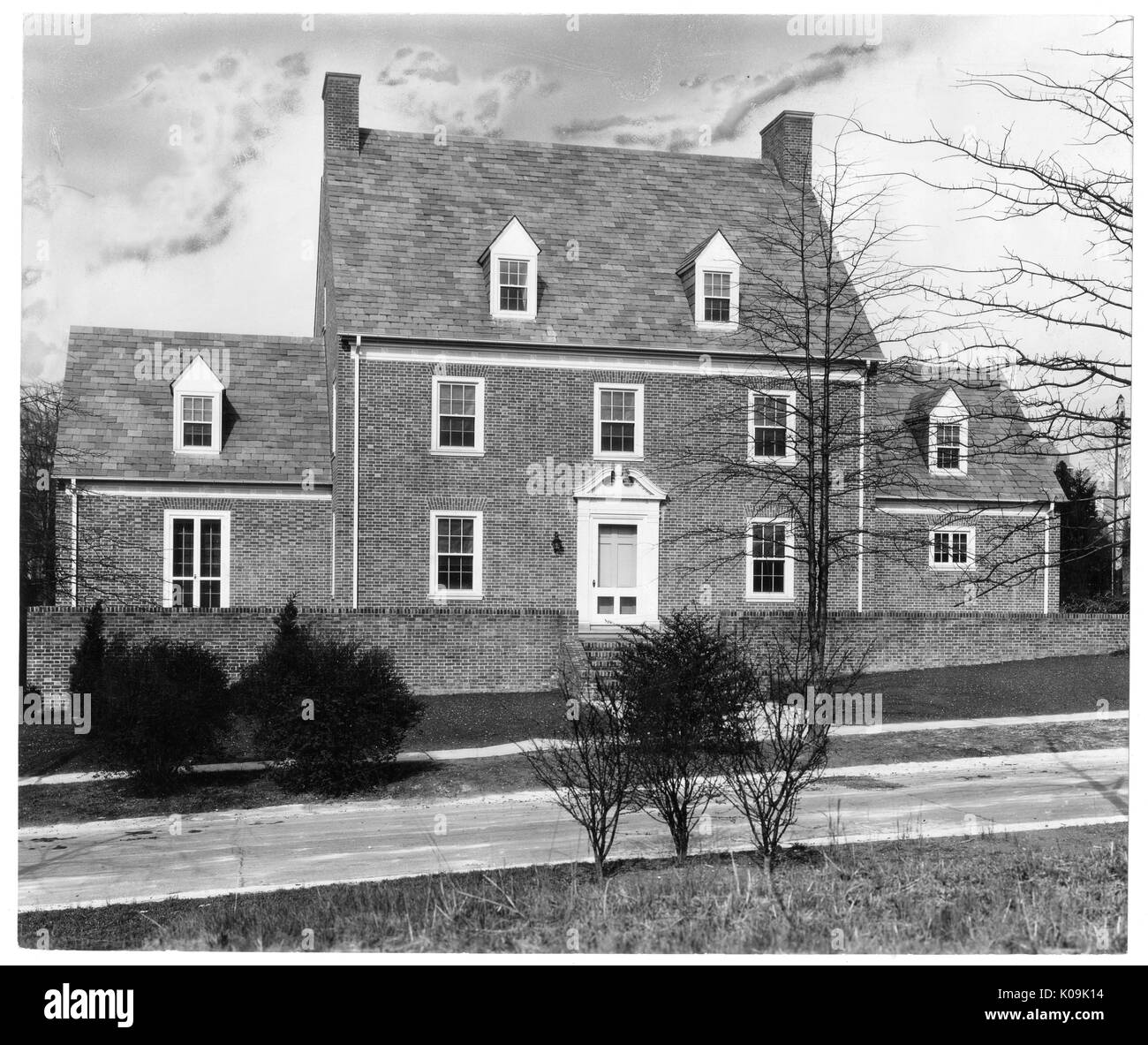 Front angle view of a single family brick house near Guilford, the house has attached rooms on both sides and a fence made of brick that lines the perimeter of the front of the house, Baltimore, Maryland, 1910. This image is from a series documenting the construction and sale of homes in the Roland Park/Guilford neighborhood of Baltimore, a streetcar suburb and one of the first planned communities in the United States. The neighborhood was segregated, and is considered an early example of the enforcement of racial segregation through the use of restricted covenants. Stock Photo