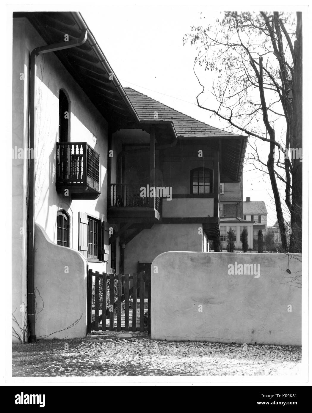 Portrait shot of the back of a house with a side gate leading to the backyard, the back of the house complex with many balconies, Roland Park/Guilford, Baltimore, Maryland, 1910. This image is from a series documenting the construction and sale of homes in the Roland Park/Guilford neighborhood of Baltimore, a streetcar suburb and one of the first planned communities in the United States. The neighborhood was segregated, and is considered an early example of the enforcement of racial segregation through the use of restricted covenants. Stock Photo