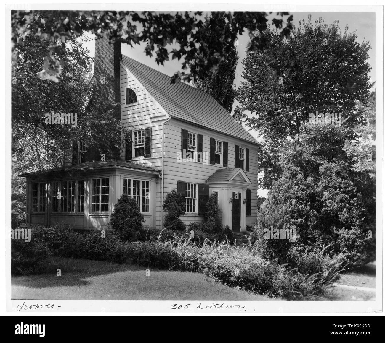 Landscape diagonal shot of a white house with an annexed sun room, surrounded by many trees and shrubs with leaves, Roland Park/Guilford, Baltimore, Maryland, 1910. This image is from a series documenting the construction and sale of homes in the Roland Park/Guilford neighborhood of Baltimore, a streetcar suburb and one of the first planned communities in the United States. The neighborhood was segregated, and is considered an early example of the enforcement of racial segregation through the use of restricted covenants. Stock Photo