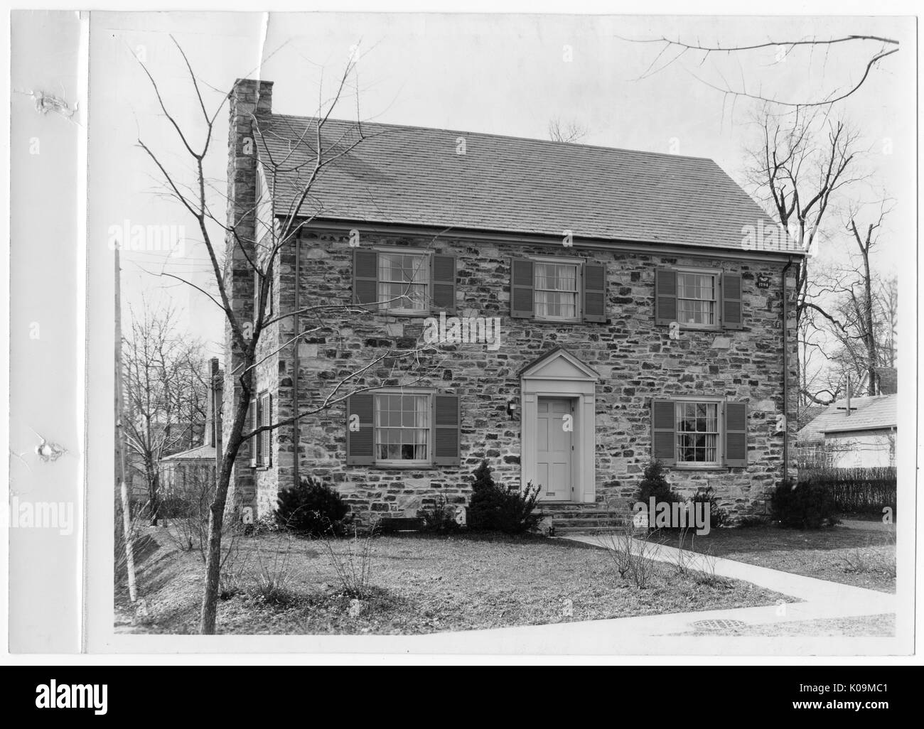 Landscape shot of a two-story brick house with a chimney, a paved sidewalk and path leading to the front door, sparse landscaping in front of the house, Roland Park/Guilford, Baltimore, Maryland, 1910. This image is from a series documenting the construction and sale of homes in the Roland Park/Guilford neighborhood of Baltimore, a streetcar suburb and one of the first planned communities in the United States. The neighborhood was segregated, and is considered an early example of the enforcement of racial segregation through the use of restricted covenants. Stock Photo