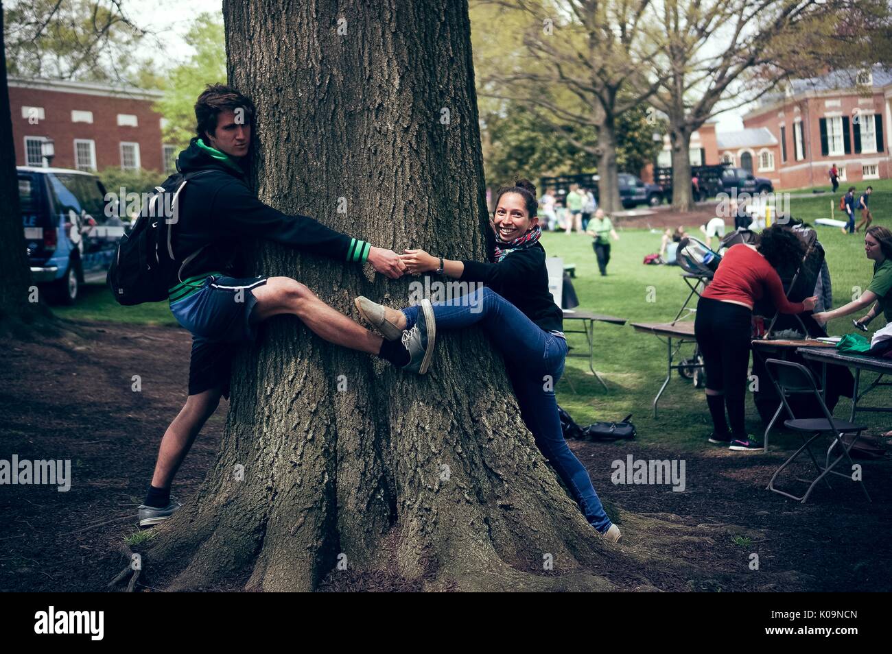 Two college students each wrap one leg and one arm around a large tree in order to have their feet and hands touch, 2015. Courtesy Eric Chen. Stock Photo
