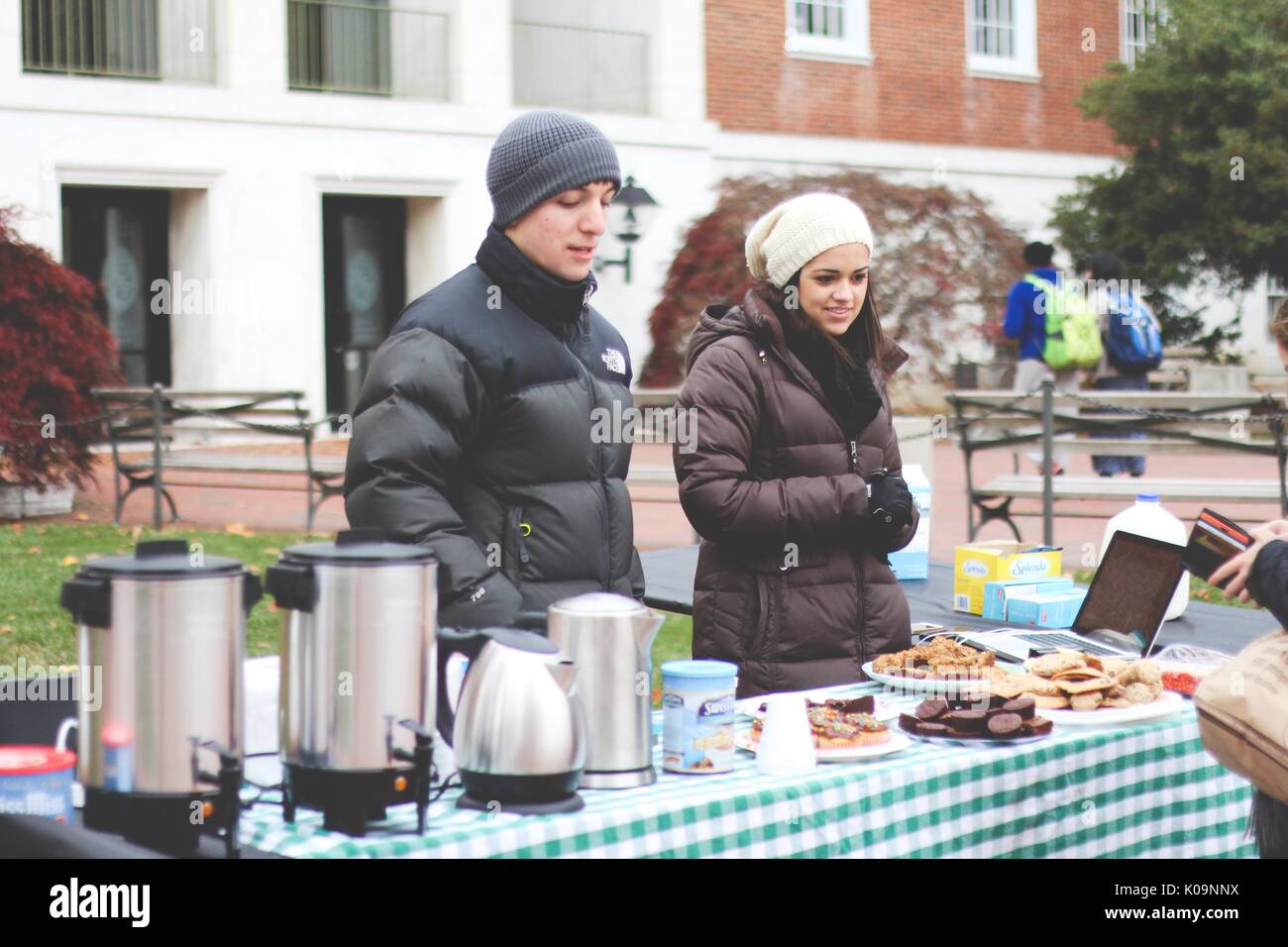 Two college students stand in front of a table with warm beverages and baked goods to sell to their peers in front of the Milton S. Eisenhower Library on the Homewood campus of Johns Hopkins University, 2015. Courtesy Eric Chen. Stock Photo