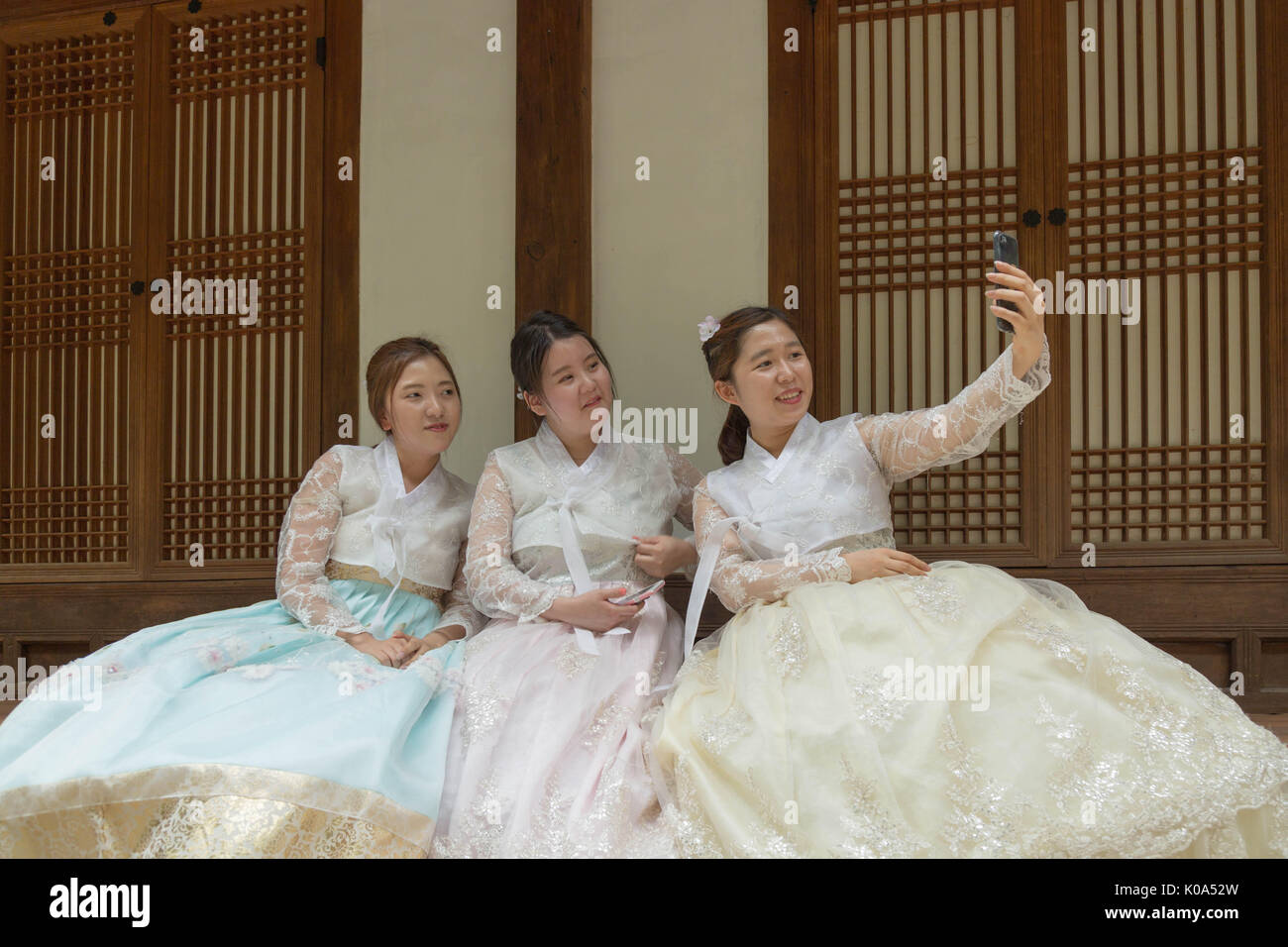 Three young women in traditional Korean outfit pose for a selfie in front of a traditional house in Seoul, South Korea. Stock Photo