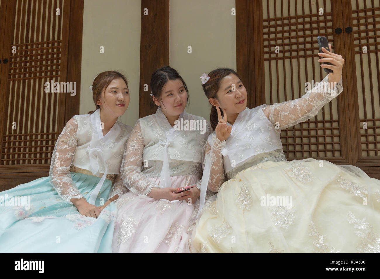 Three young women in traditional Korean outfit pose for a selfie in front of a traditional house in  Seoul, South Korea. Stock Photo