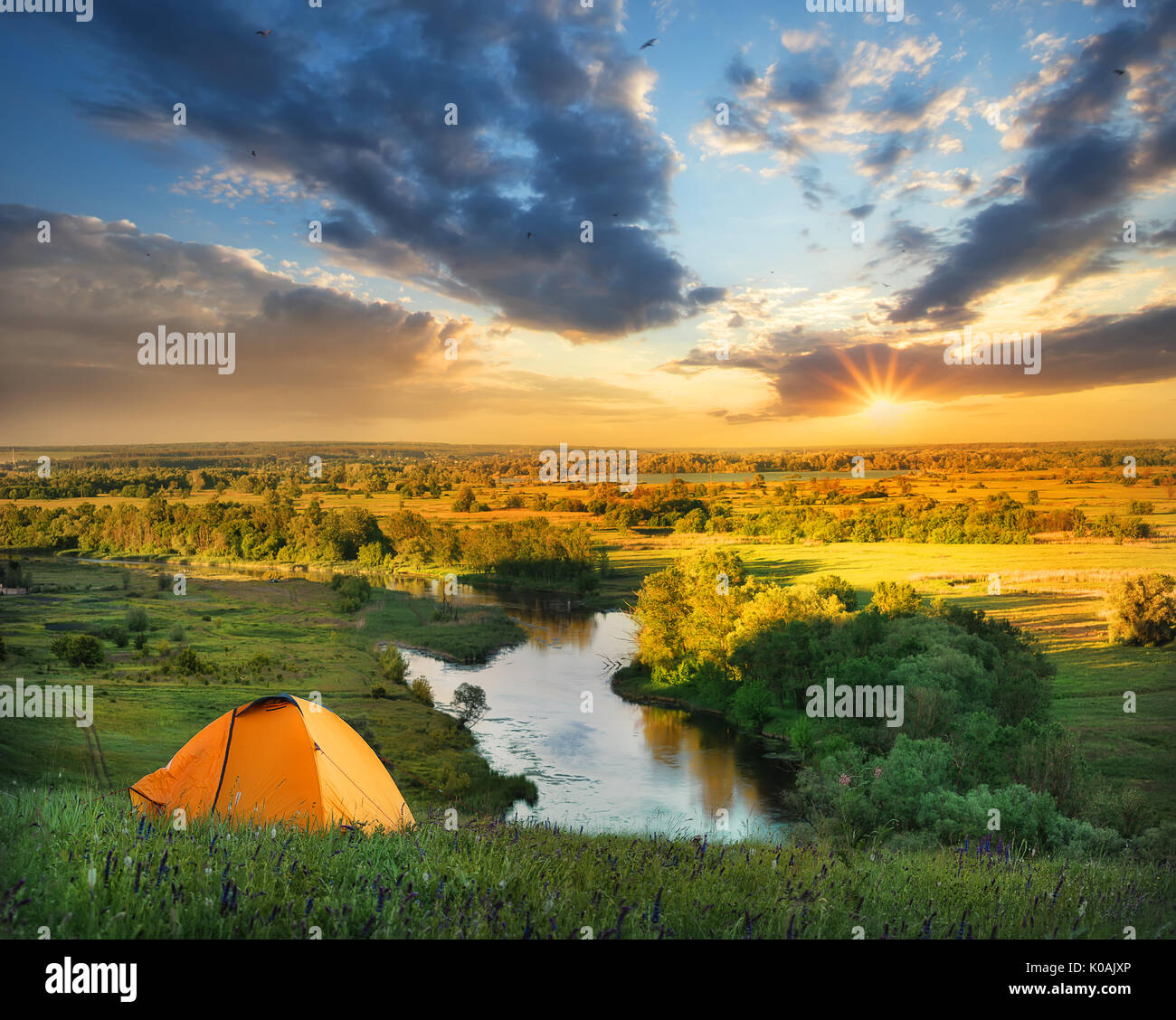 River under a hill with an orange tent at sunset Stock Photo