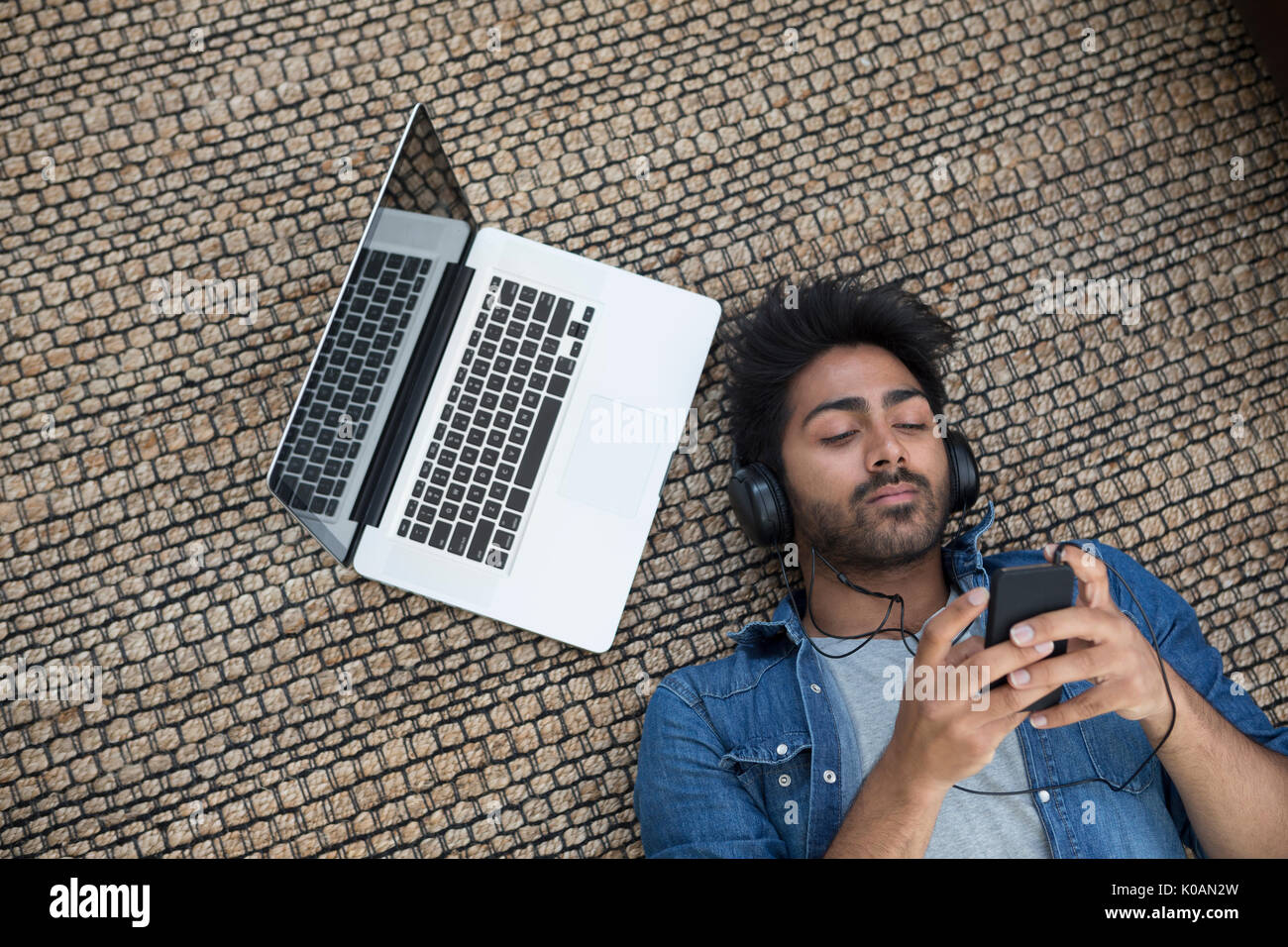 Asian man lying on the floor at home with laptop and phone. Above view Stock Photo