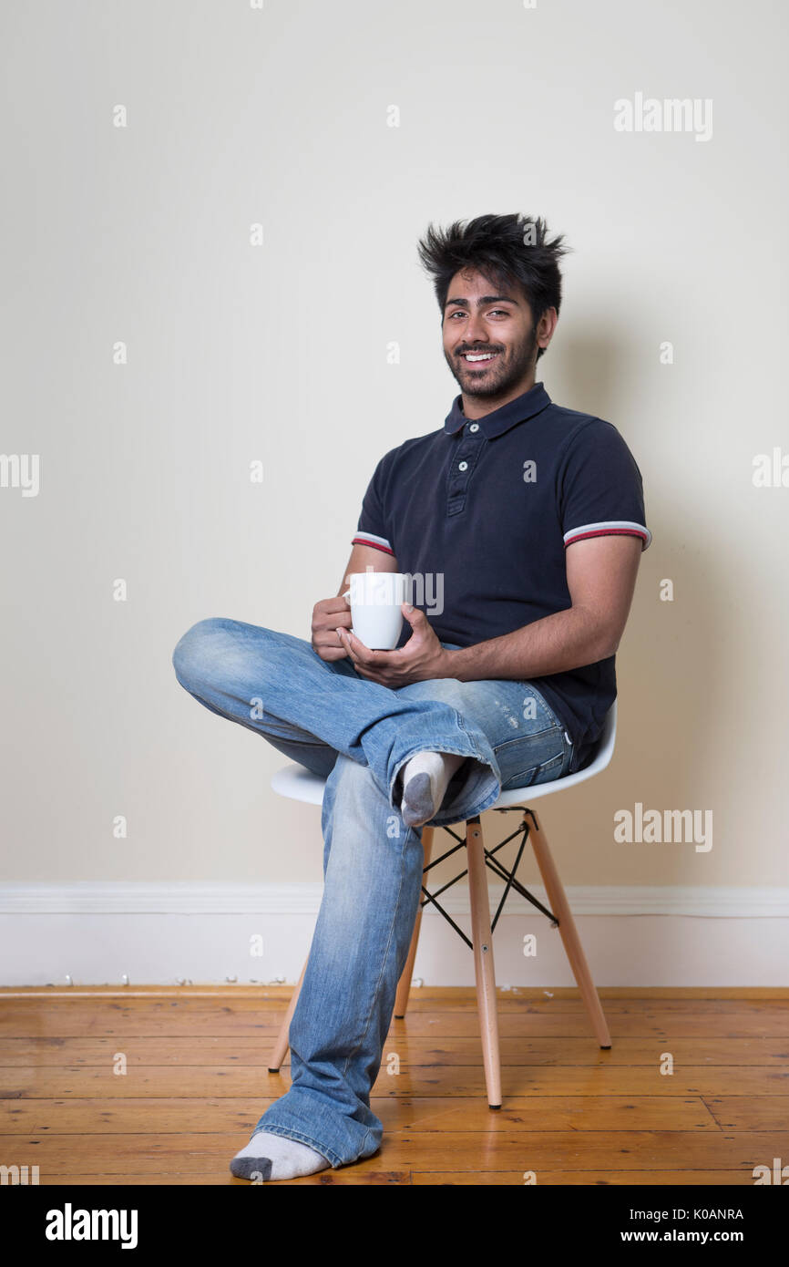Portrait of a happy Indian man sitting on a chair with a cup of coffee ...