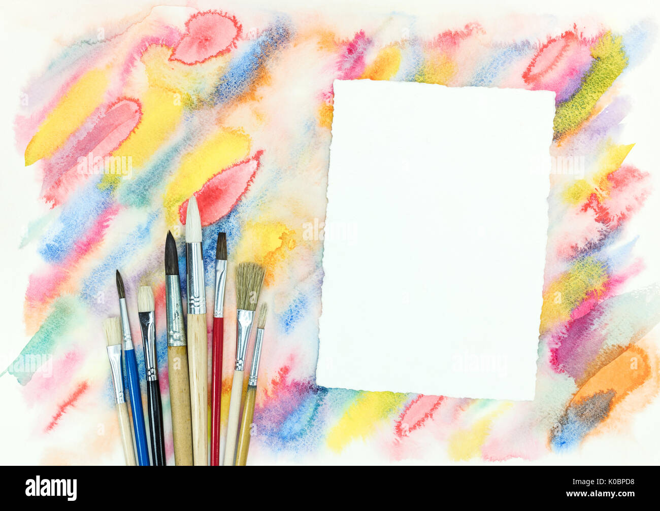 empty paper sheet with various paintbrushes over colorful diagonal watercolor strokes background Stock Photo