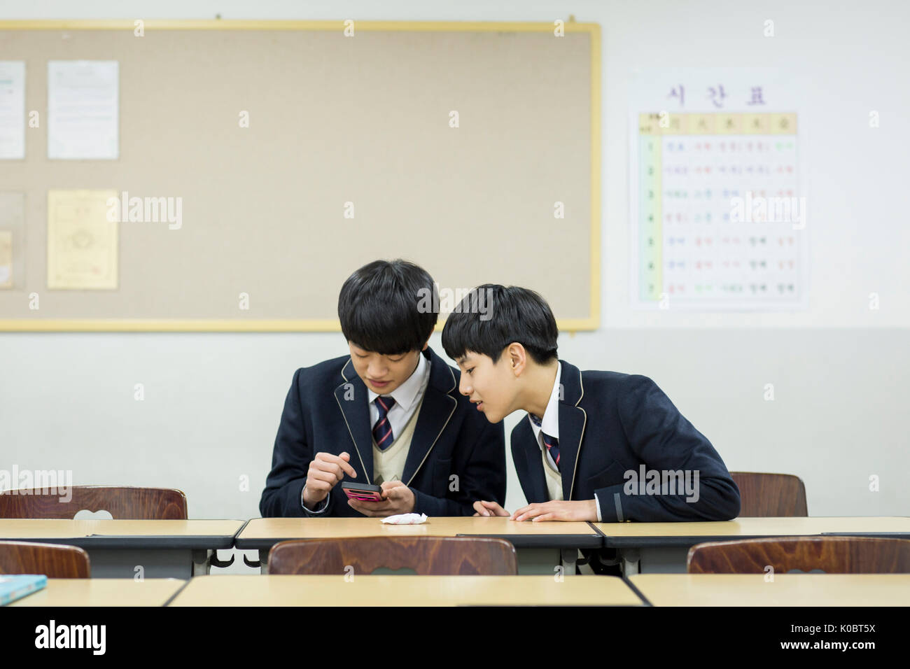 Portrait of two school boys sharing a smartphone in classroom Stock Photo