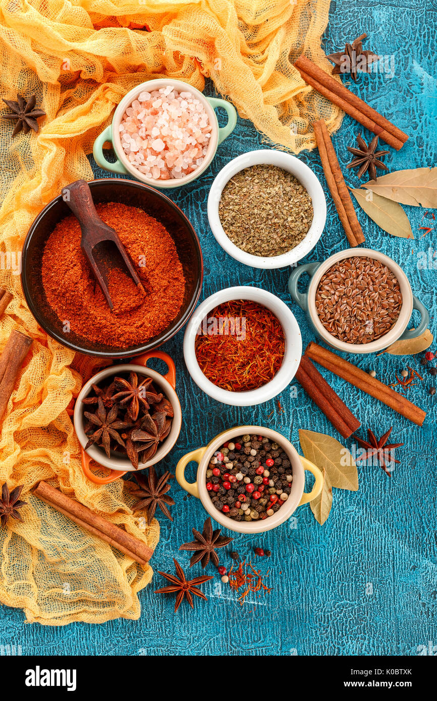 Dry colorful spices and condiments anise, paprika, saffron, pepper, salt, bay leaf, cinnamon in small bowls on blue background Stock Photo