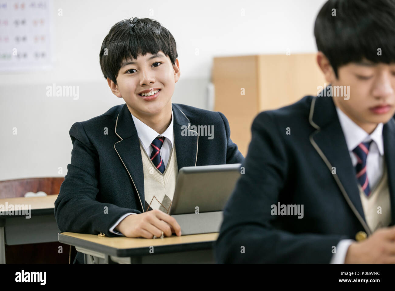Portrait of smiling school boy and his classmate with electric tablets in classroom Stock Photo