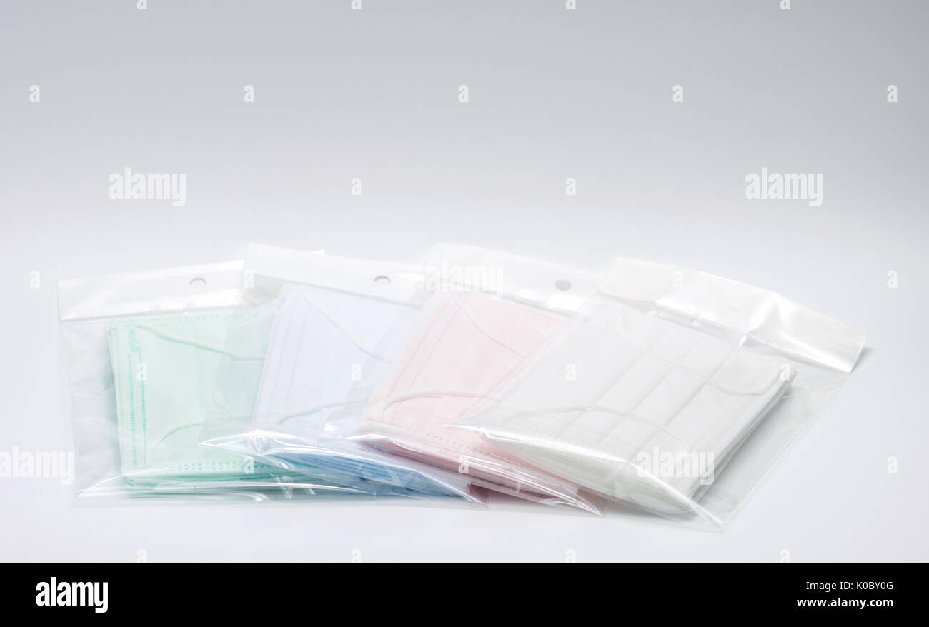 Green, pink, light blue and white ear loop disposable face mask in plastic bag overlapping, used for covering mouth and nose. It protects against body Stock Photo
