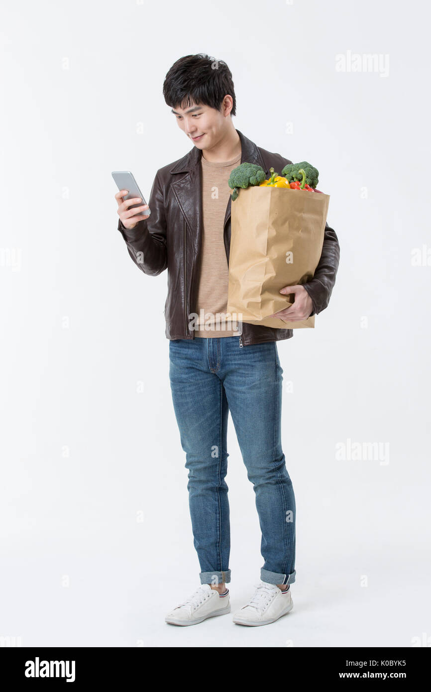 Young smiling man with shopping bag standing using smartphone Stock Photo
