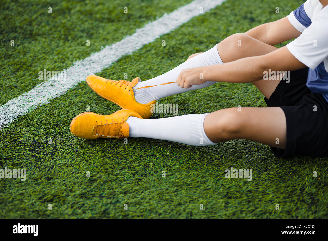 Young Soccer Player Tying Soccer Shoes on the Pitch. Football Equipment
