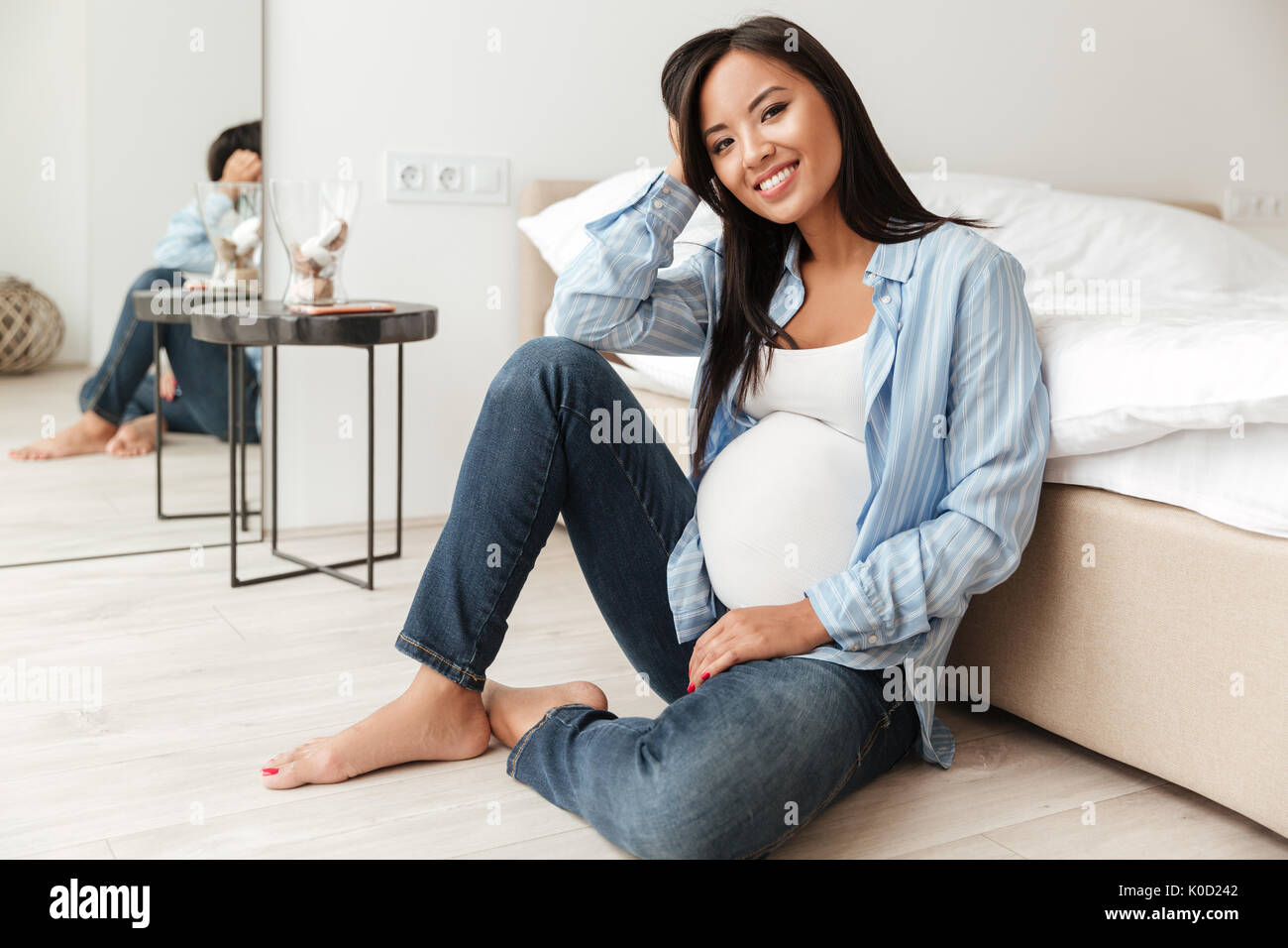 Happy Pregnant Asian Woman Leaning On A Sofa While Sitting On The