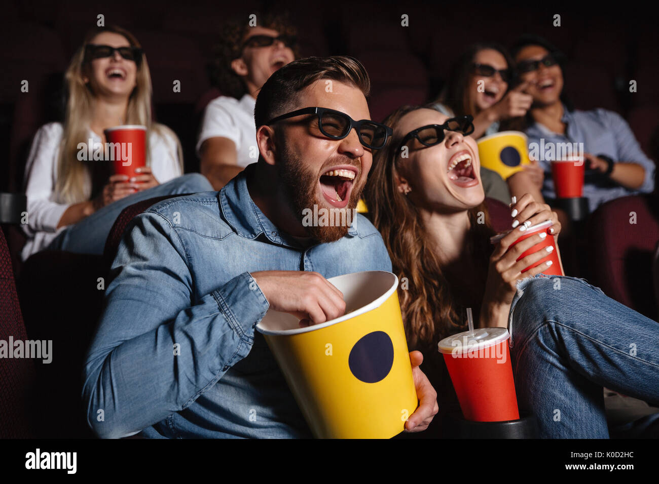 Image of laughing friends sitting in cinema watch film eating popcorn