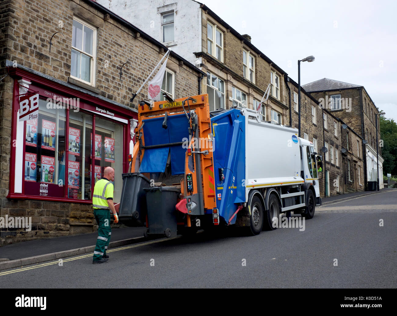 A refuse disposal lorry unloads a wheelie bin outside Bargain Booze. Stock Photo