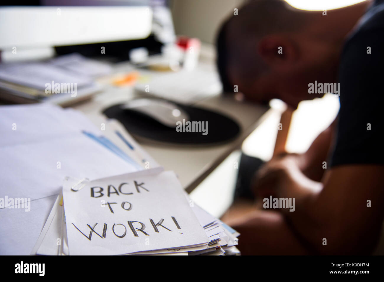 closeup of a concerned man sitting at his office desk and a note in the foreground with the text back to work handwritten in it Stock Photo