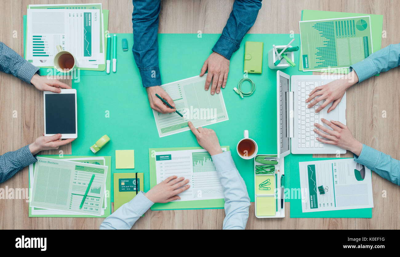 Business people working together on a green desktop and examining a report; environment, green business and finance concept Stock Photo