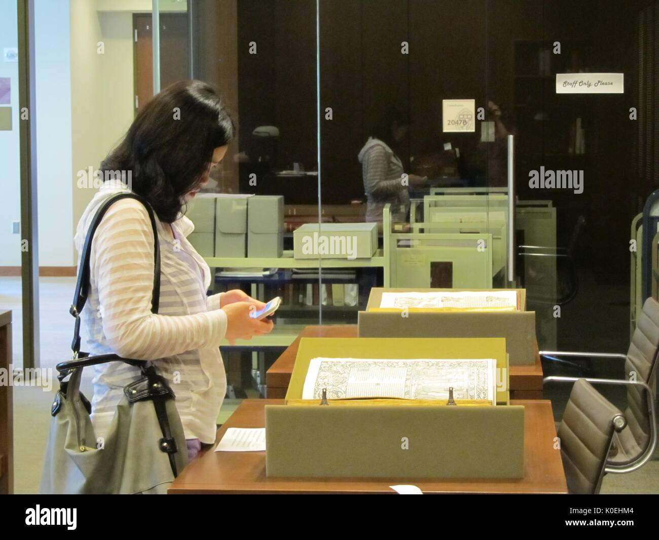 A student on her phone stands over a rare object from Johns Hopkins University's Special Collections a the Special Collections Open House 2014, on the Homewood campus of the university in Baltimore, Maryland, 2014. Courtesy Eric Chen. Stock Photo