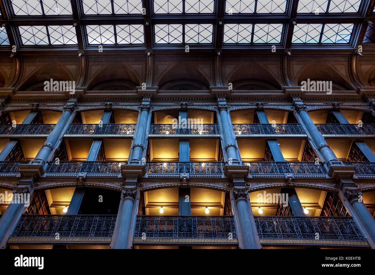 A low-angle shot of the levels of the George Peabody Library, a research library for Johns Hopkins University, with cast iron railings and exposed glowing light bulbs lighting the full bookshelves during the Baltimore Book Festival, Baltimore, Maryland, September 28, 2013. Courtesy Eric Chen. Stock Photo