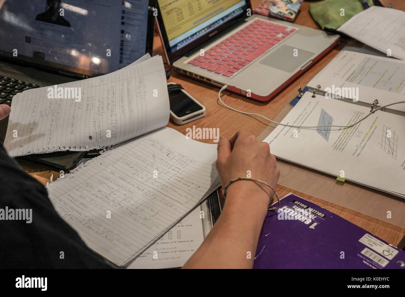A close-view shot of a college student reviewing Calculus homework at a table, only their arm and hand visible, with another set of notes from a Calculus textbook to the right, and a laptop behind each pile of study materials, with cellular phones and notebooks scattered across the table, Johns Hopkins University, Baltimore, Maryland, 2014. Courtesy Eric Chen. Stock Photo