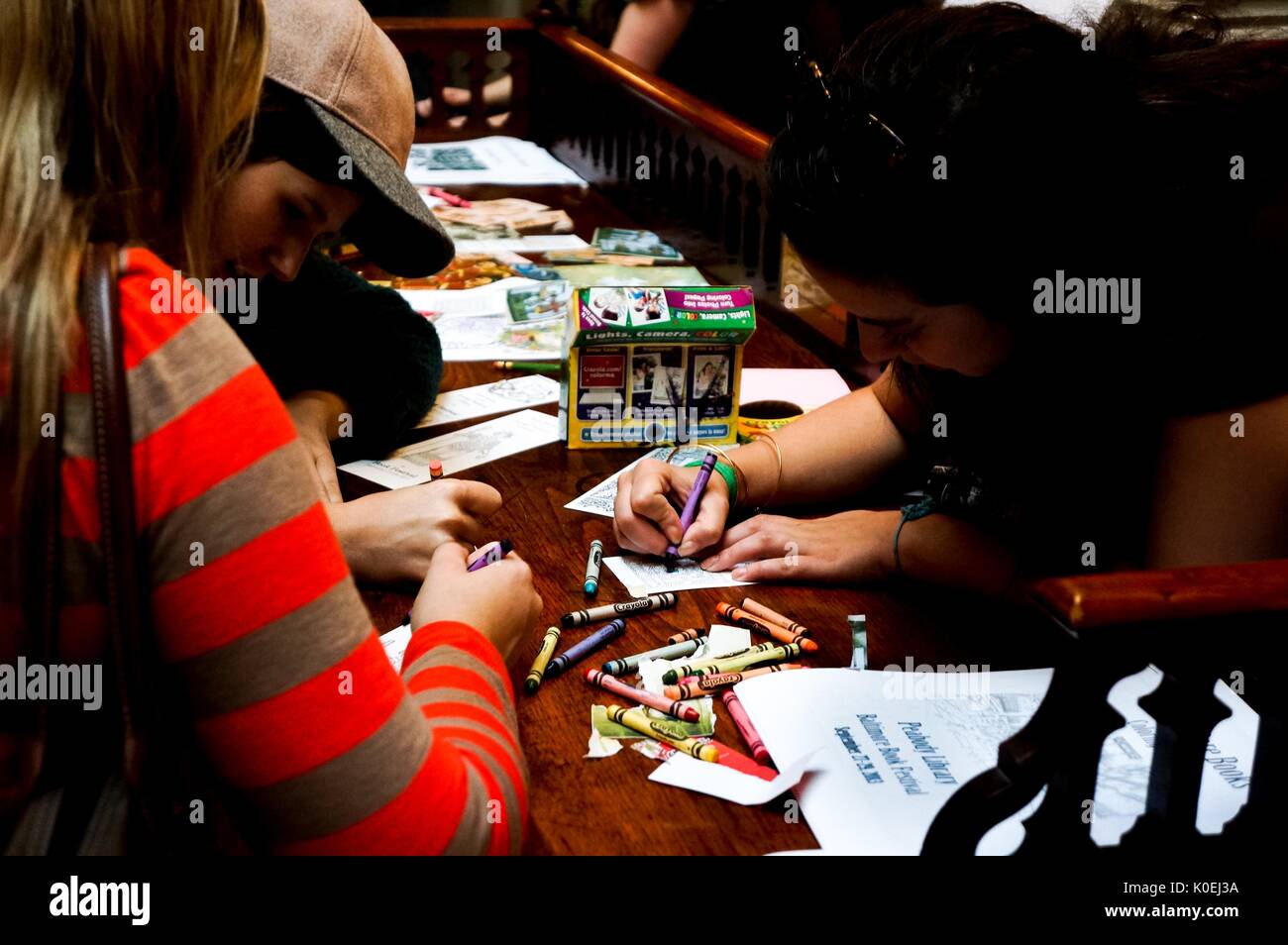 College students sit at an old wooden desk coloring bookmarks with crayons at the Baltimore Book Festival, a large festival where authors and readers come together for signings and readings, hosted at the historic George Peabody Library at Johns Hopkins University, Baltimore, Maryland, 2013. Courtesy Eric Chen. Stock Photo