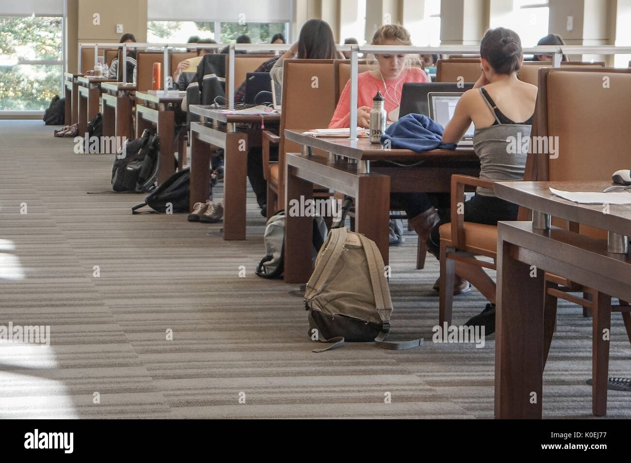 A shot down the sunny aisle of the Albert Hutzler Reading Room, a two-story silent reading room in the Brody Learning Commons of Johns Hopkins University; college students work at rows of tables with laptops and backpacks all around them; Baltimore, Maryland, March, 2014. Courtesy Eric Chen. Stock Photo