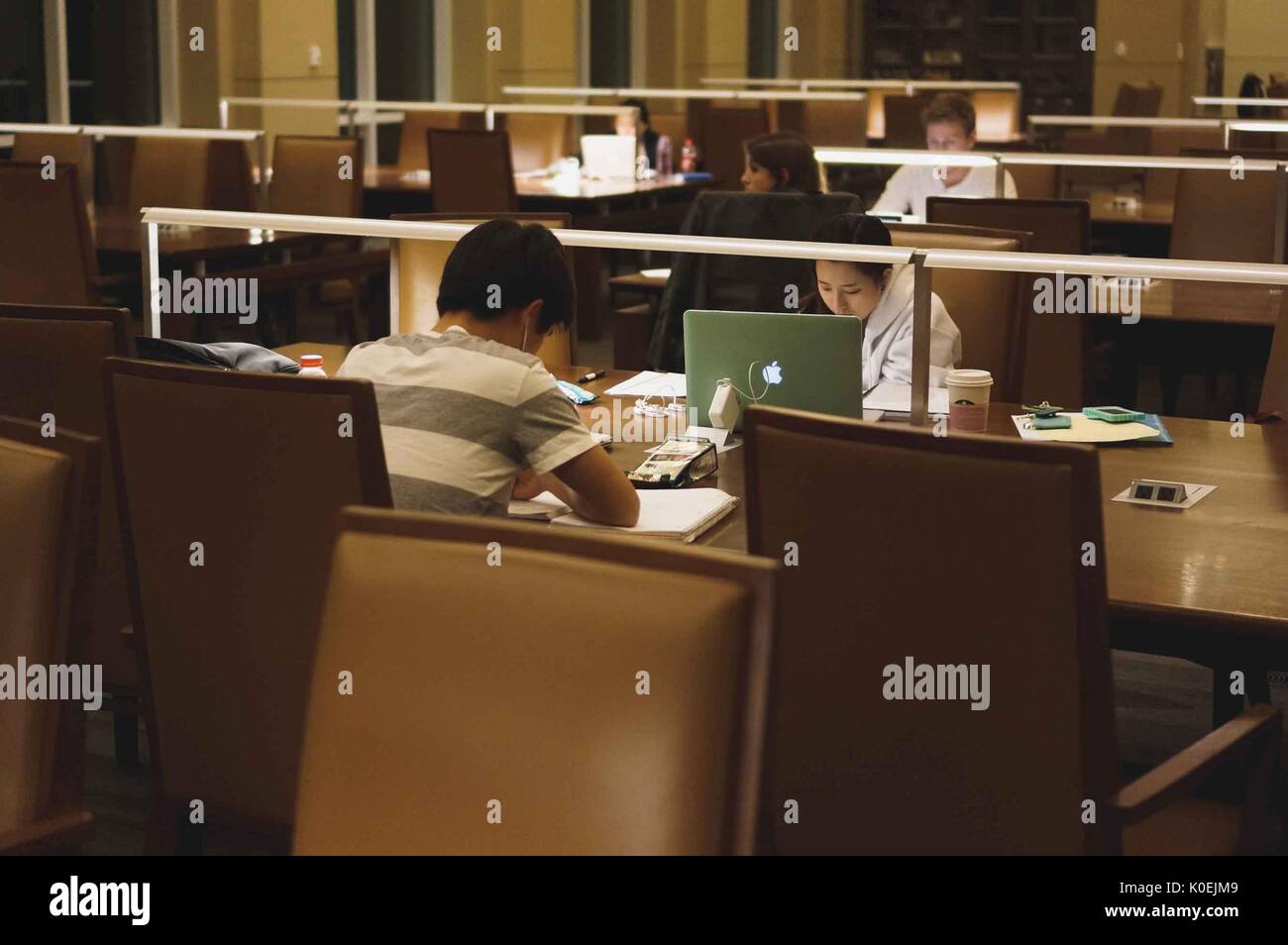 College students seated at study tables work from notebooks and laptops during the late hours of the night, the only light in the dim room coming from lamps on the tables, Albert Hutzler Reading Room, Brody Learning Commons, Johns Hopkins University, Baltimore, Maryland, March, 2014. Courtesy Eric Chen. Stock Photo