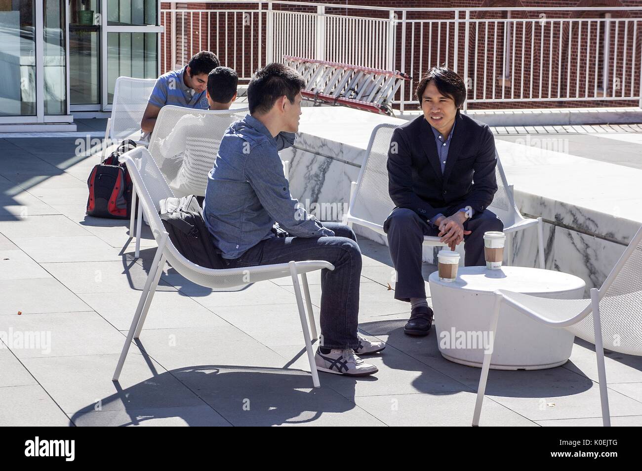 College students sit, socialize, and drink coffee on the patio area outside of the Brody Learning Commons, an interactive/collaborative study space and library on the Homewood campus of the Johns Hopkins University in Baltimore, Maryland. 2014. Courtesy Eric Chen. Stock Photo