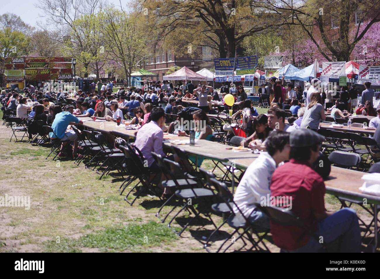 College students and members of the Johns Hopkins and Baltimore communities sit at tables, eating and socializing as food stands surround them, during Spring Fair, an annual festival with music, food, shopping, and more that takes place every spring on the Homewood campus of the Johns Hopkins University in Baltimore, Maryland. 2014. Courtesy Eric Chen. Stock Photo