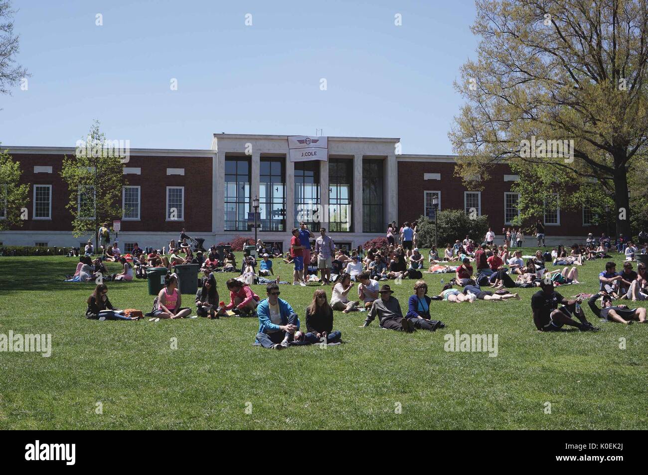 College students and members of the Johns Hopkins and Baltimore communities sit on the beach, a large grassy area in front of the Milton S. Eisenhower Library, during Spring Fair, an annual festival with music, food, shopping, and more that takes place every spring on the Homewood campus of the Johns Hopkins University in Baltimore, Maryland. 2014. Courtesy Eric Chen. Stock Photo