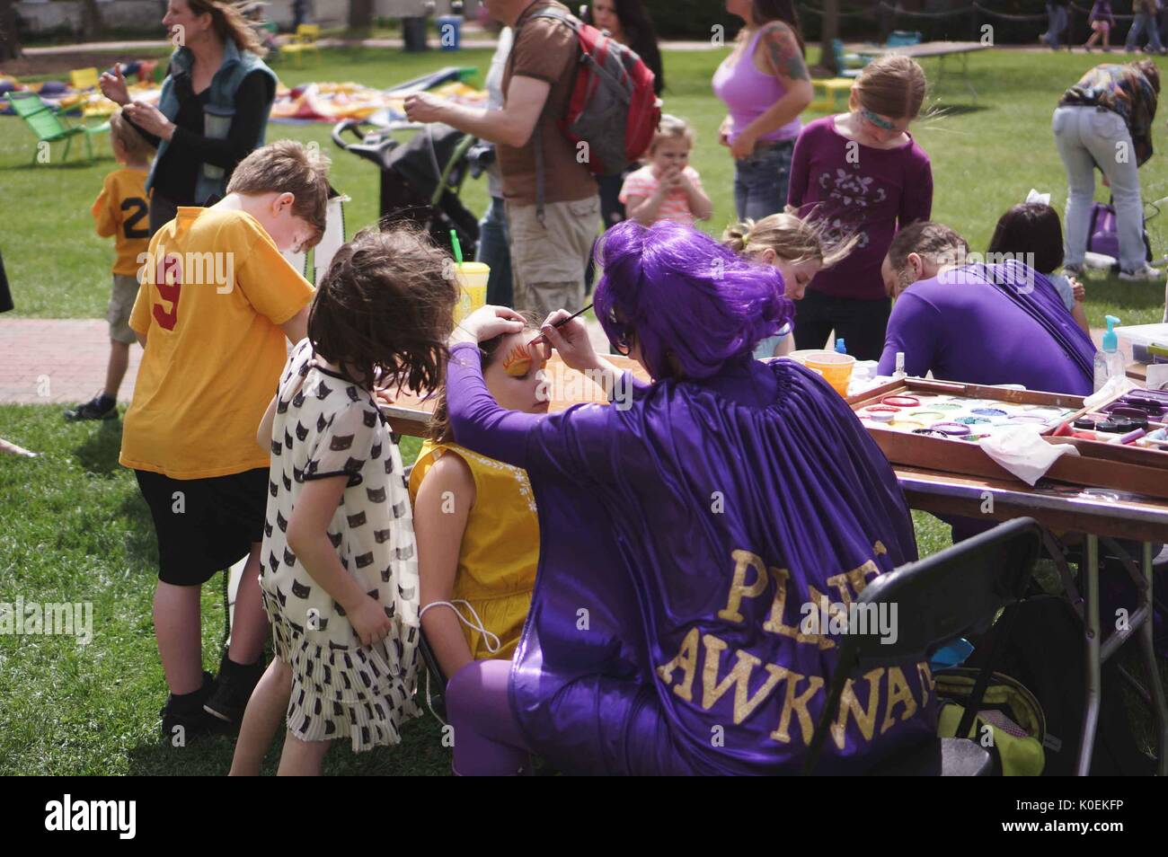 A woman and man wearing purple superhero costumes, including cape and wig, paint designs onto the faces of young children during Spring Fair, a student-run spring carnival at Johns Hopkins University, Baltimore, Maryland, April, 2014. Courtesy Eric Chen. Stock Photo