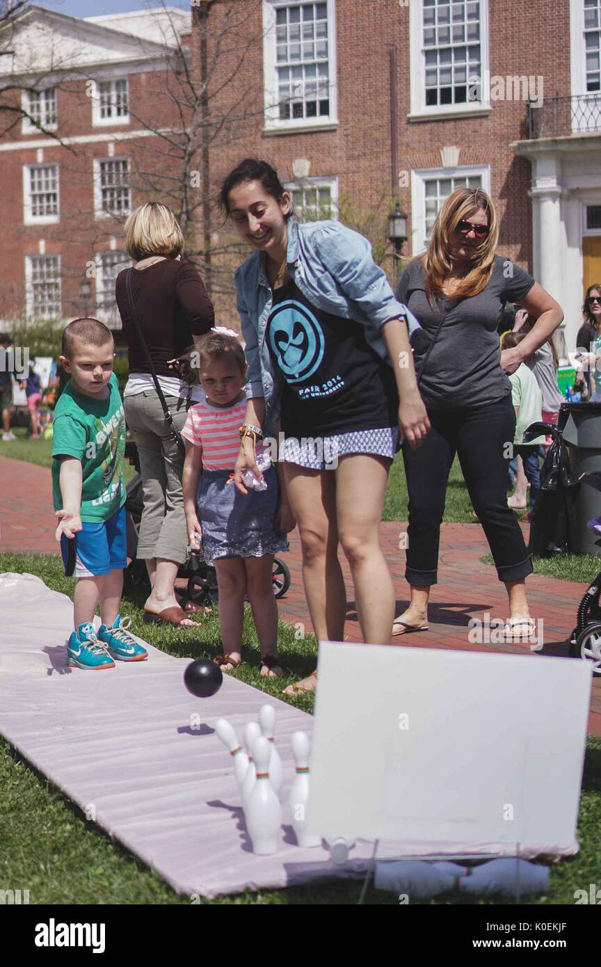 A young boy bowls with duckpins as a young girl, female student, and mother watch, during Spring Fair, a student-run spring carnival at Johns Hopkins University, Baltimore, Maryland, April, 2014. Courtesy Eric Chen. Stock Photo