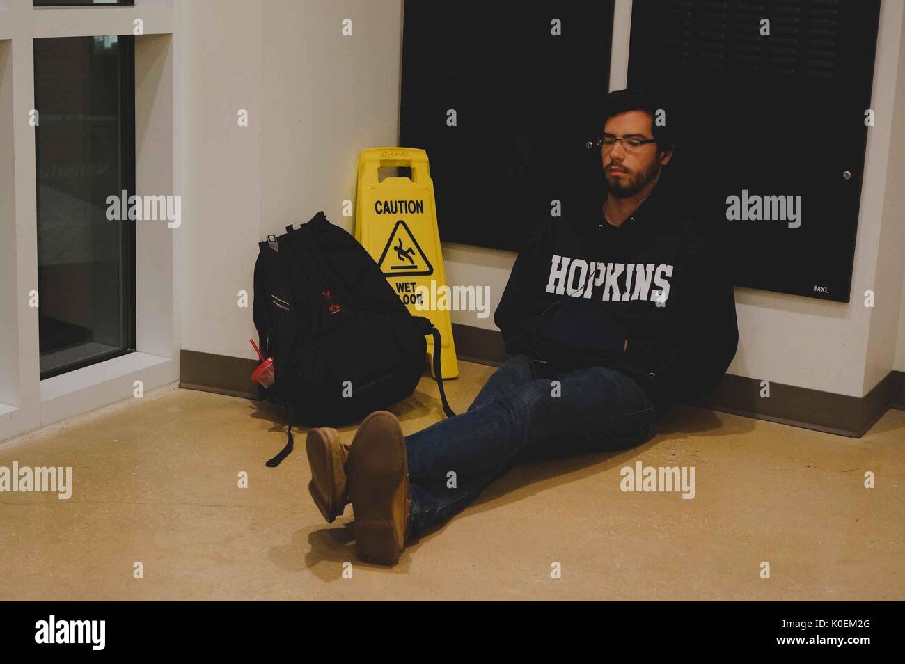 A college student taking a nap while siting against a wall in Brody Learning Commons, his backpack and a Caution Wet Floor sign sit beside him, 2014. Courtesy Eric Chen. Stock Photo