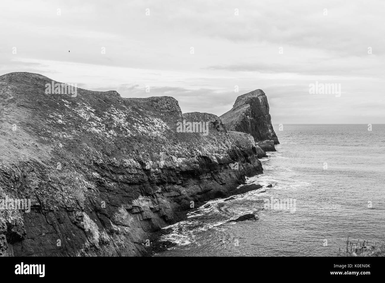 A black and white coastal scene with sea, sun sand and rock with the Worms Head at Rhossili Bay on the Gower Peninsula in Wales, UK Stock Photo