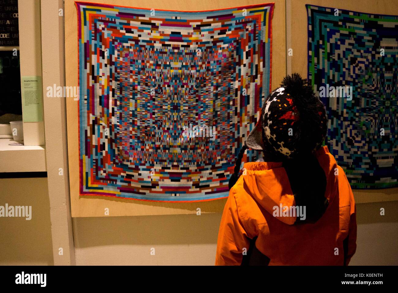 A college student looks on at a colorful piece of artwork that hangs on a wall at the Unravel the Code Opening at The Johns Hopkins University Sheridan Libraries, 2016. Courtesy Eric Chen. Stock Photo